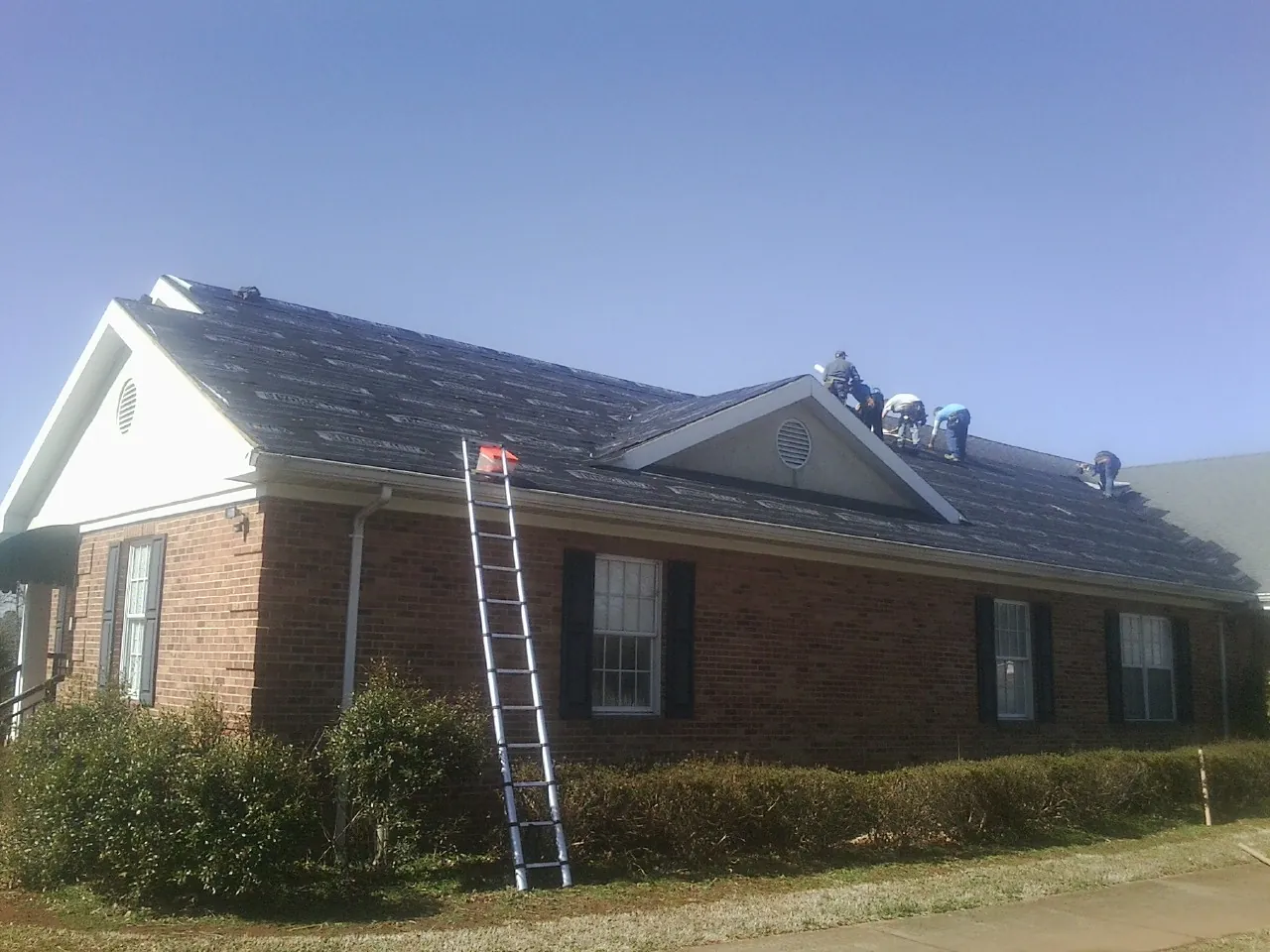 Crew tearing shingles off a brick ranch roof with a ladder set — Emergency Roof Repair work by our crew in Chester Springs