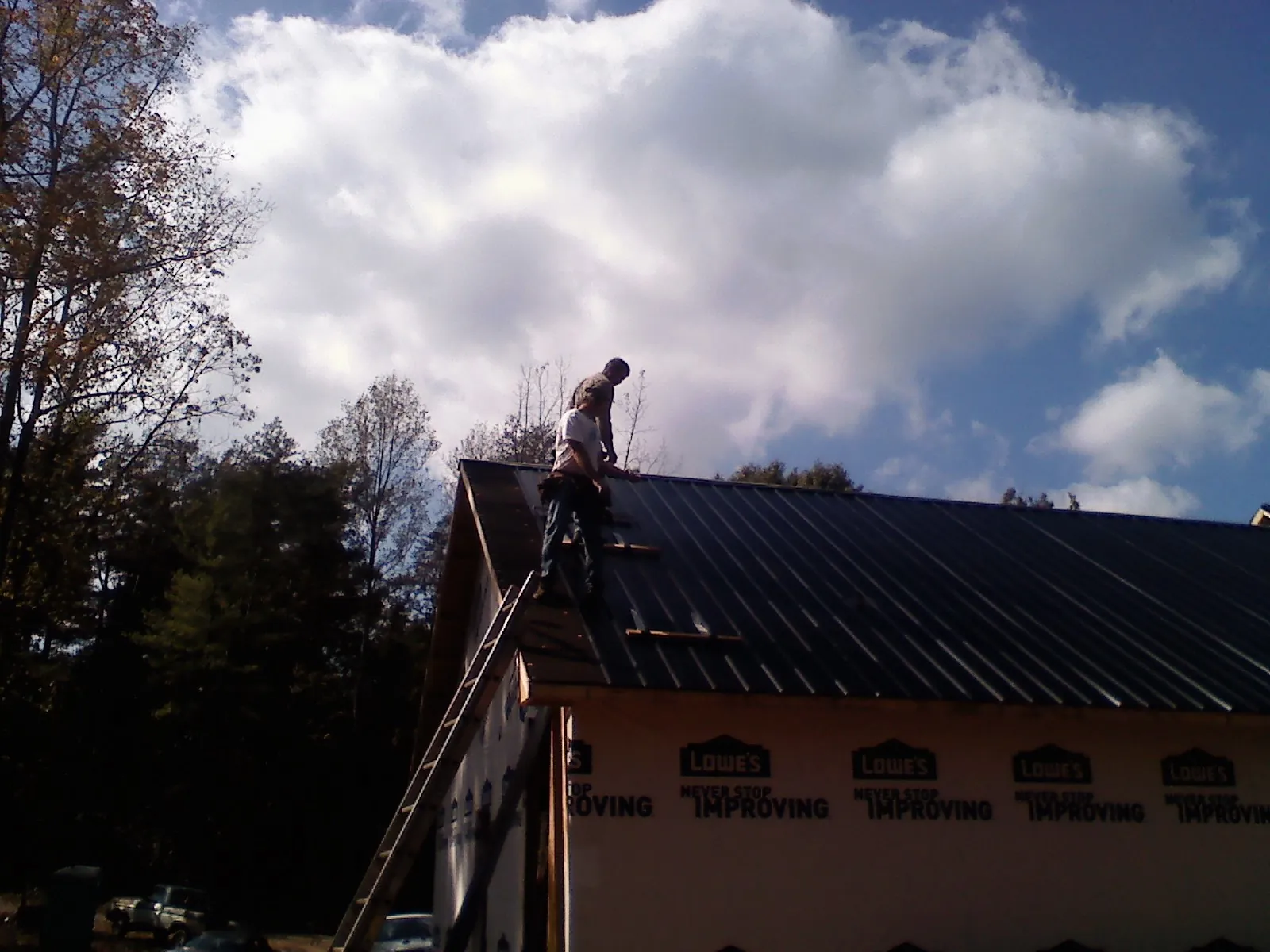 Roofer fastening dark metal panels high against a cloudy sky, from a Roof Inspection job in Chester Springs