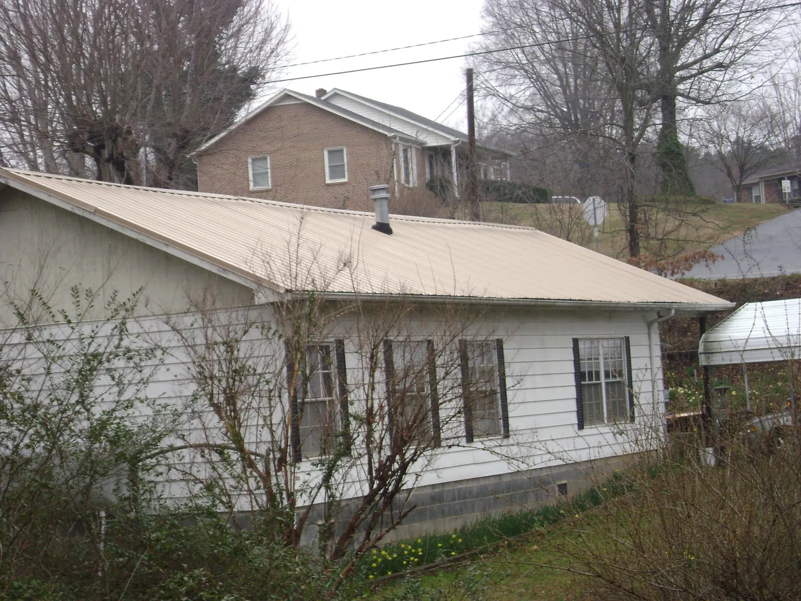 Tan metal roof on a white sided house set into a hillside — Commercial Roofing by Roofing Brothers in Chester Springs